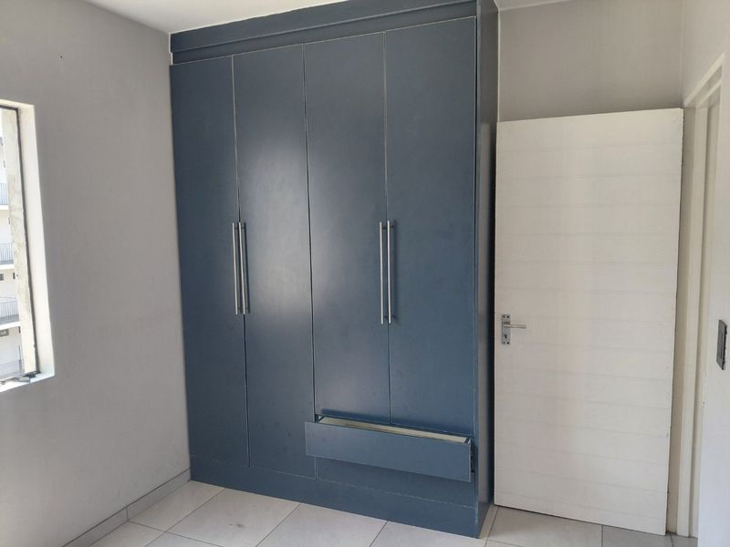 A bedroom featuring a large built-in blue wardrobe with a damaged drawer front, tiled flooring, and a white internal door.