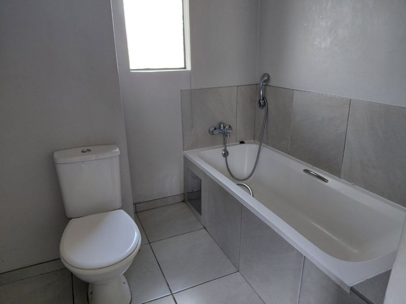 A functional bathroom featuring a bathtub with a shower mixer, a standard toilet, and neutral wall and floor tiling.