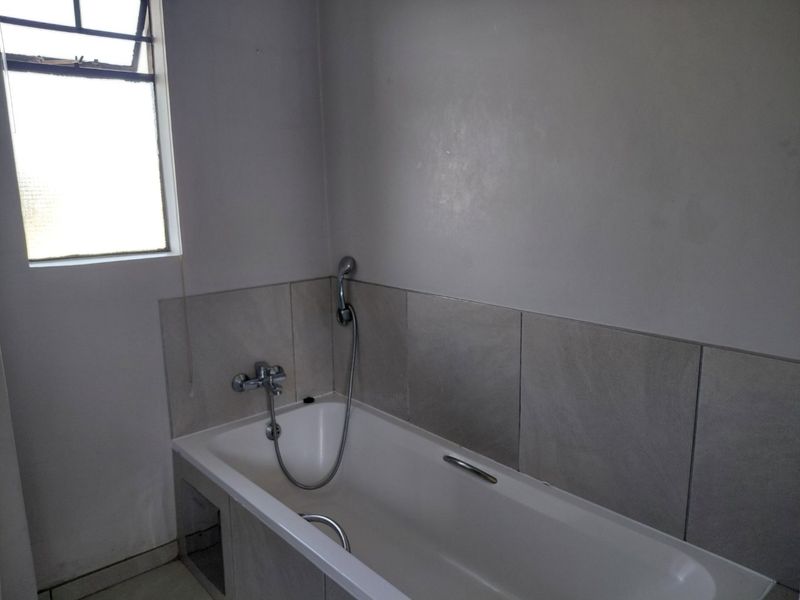 A functional bathroom featuring a bathtub with a handheld shower mixer and neutral wall tiling.
