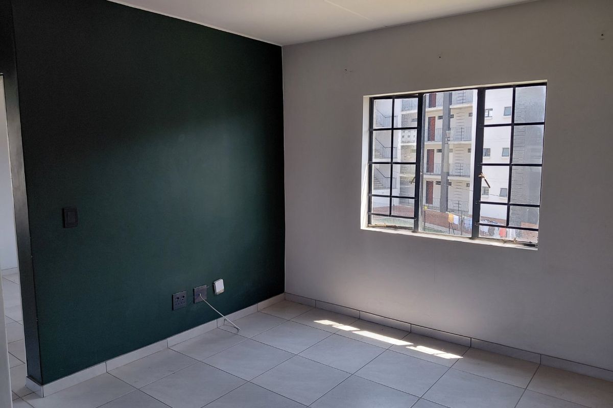 An empty bedroom featuring tiled flooring, a dark green accent wall, and a window fitted with security bars.