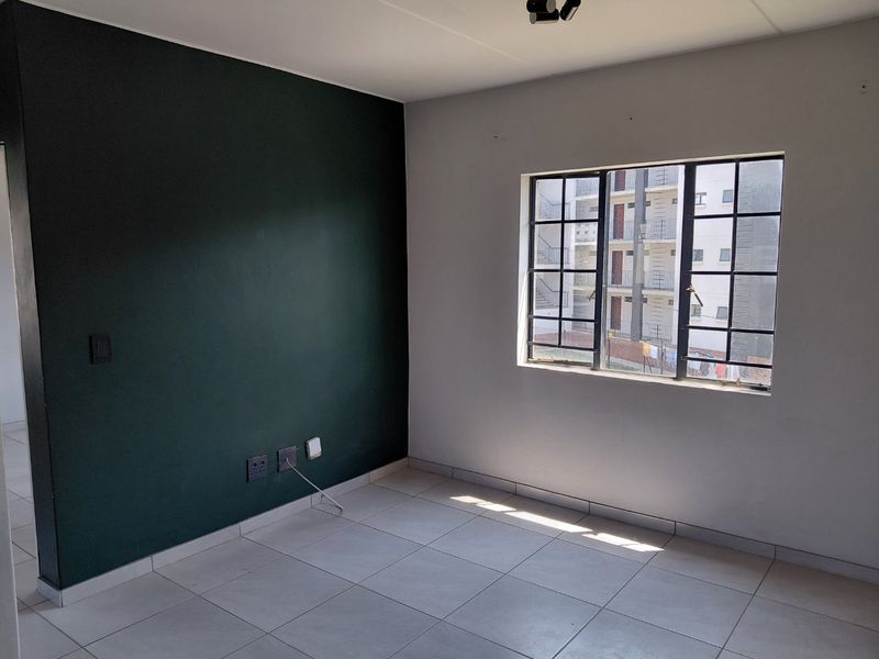 An empty bedroom featuring tiled flooring, a dark green accent wall, and a window fitted with security bars.