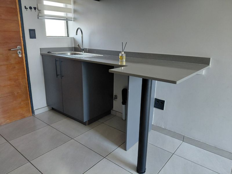 A compact, modern kitchen area featuring dark grey cabinetry, a stone countertop with an integrated sink, and a breakfast bar extension.