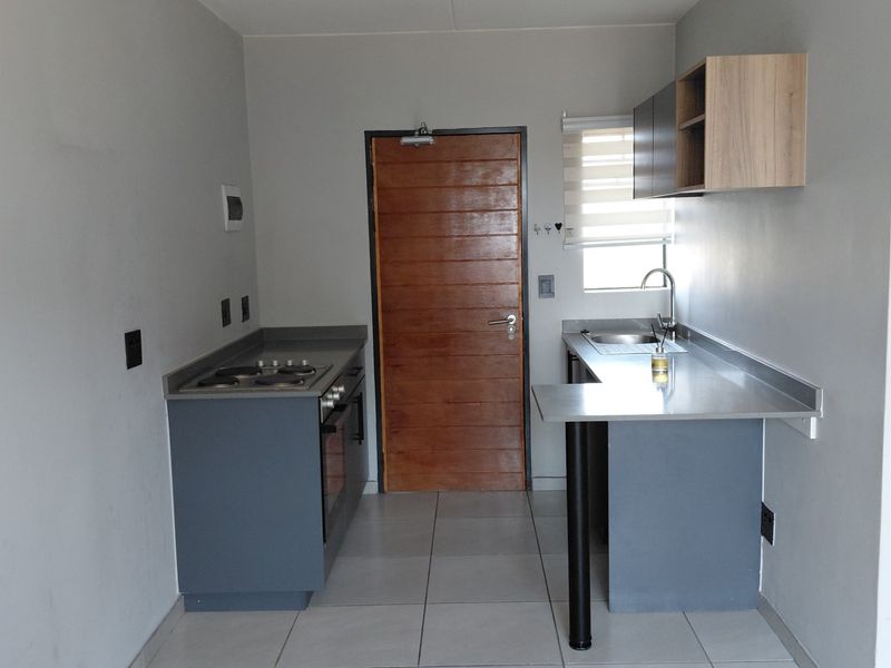 A compact, modern kitchen featuring stainless steel countertops, built-in oven and hob, tiled flooring, and neutral cabinetry, offering a clean and functional workspace.