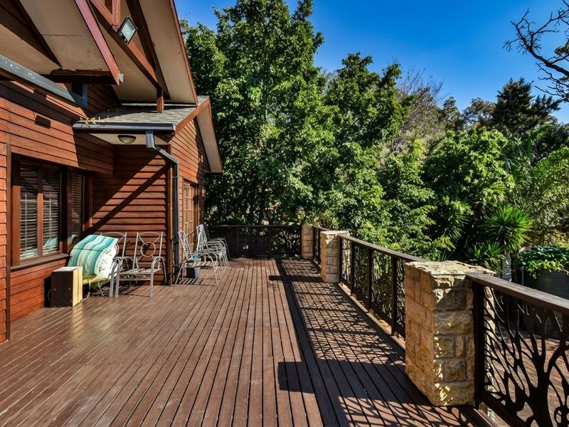 Spacious timber deck featuring stone pillars and decorative metal balustrades, offering a peaceful outdoor living area overlooking mature trees.
