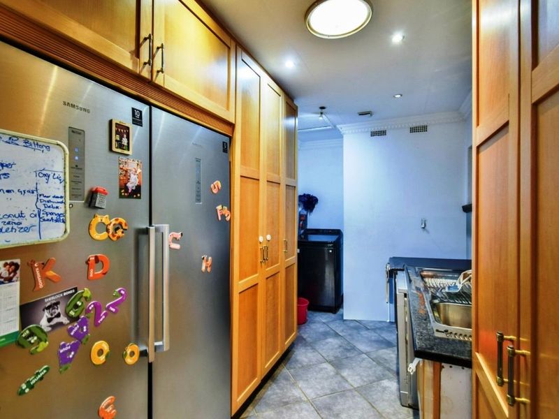 A functional scullery area featuring extensive wooden cabinetry, granite countertops, a stainless steel sink, and tiled flooring, providing additional prep and storage space.