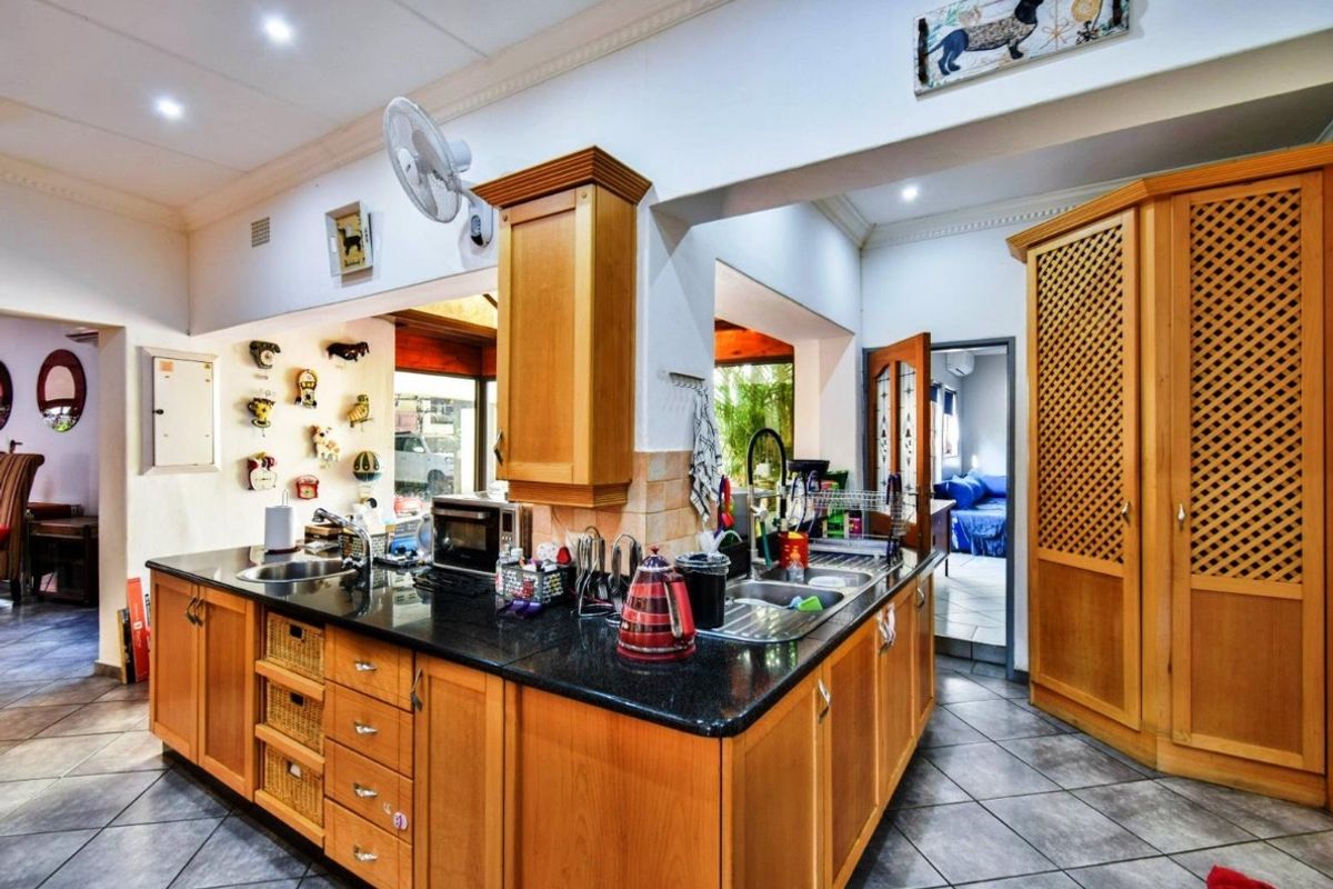 A functional kitchen featuring wooden cabinetry, granite countertops, a double sink, and tiled flooring, with an adjacent pantry and open-plan layout.