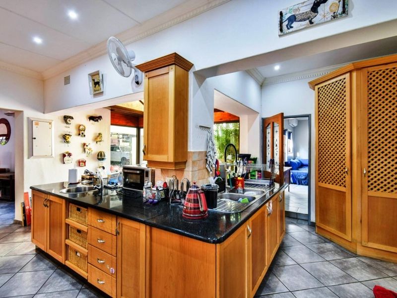 A functional kitchen featuring wooden cabinetry, granite countertops, a double sink, and tiled flooring, with an adjacent pantry and open-plan layout.