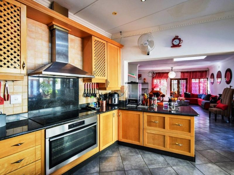 Open-plan kitchen featuring wooden cabinetry, granite countertops, and integrated appliances, flowing seamlessly into the adjacent living area with tiled flooring throughout.