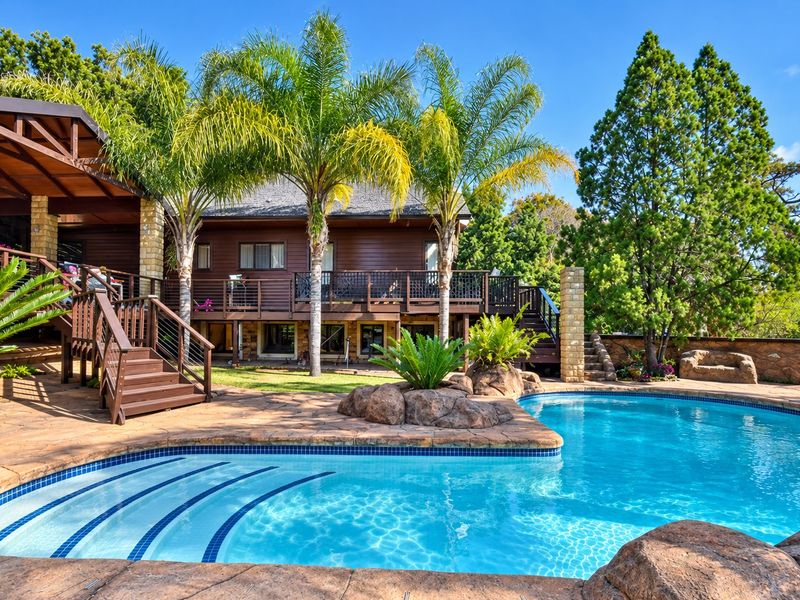 A well-maintained outdoor pool area featuring a swimming pool, stone paving, timber decking, and a covered patio area set within a landscaped garden.