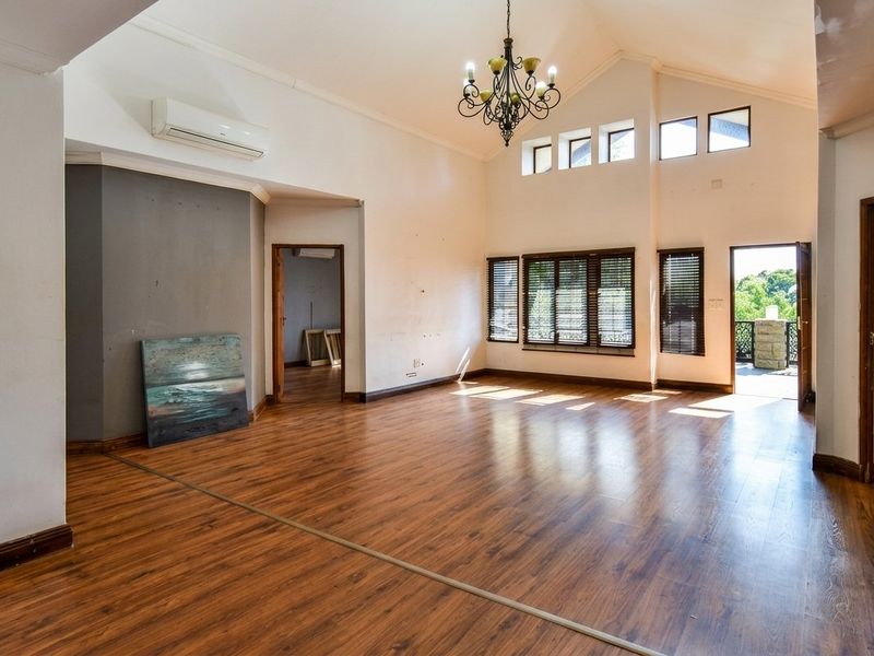 Spacious living area featuring vaulted ceilings, laminate flooring, split-system air conditioning, and abundant natural light through clerestory windows and access to an outdoor balcony.