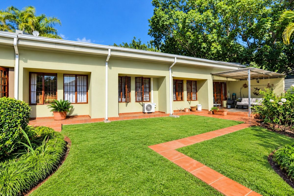 Rear view of the property featuring a well-maintained lawn, terracotta tiled patio and walkways, and timber-framed windows and doors.