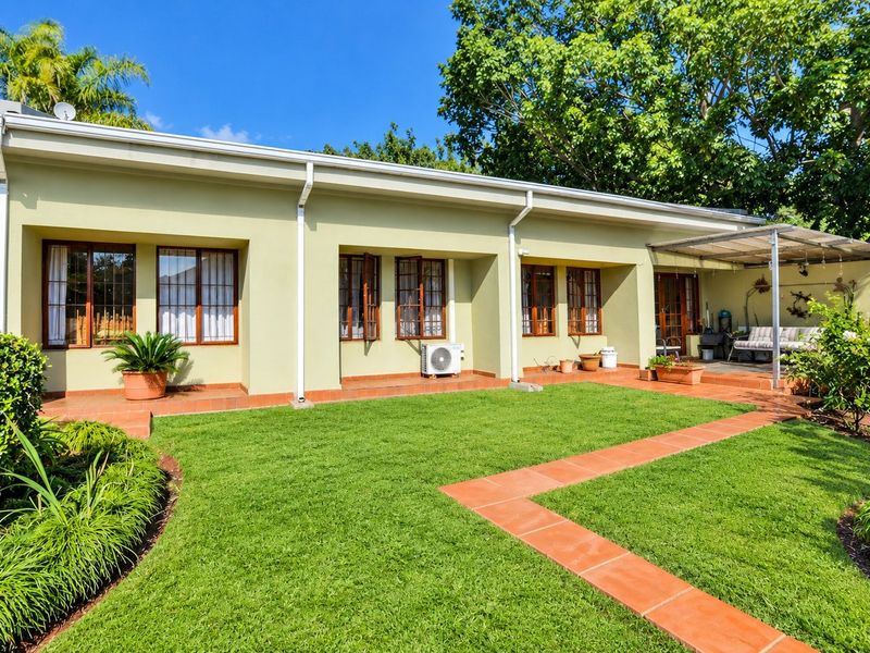 Rear view of the property featuring a well-maintained lawn, terracotta tiled patio and walkways, and timber-framed windows and doors.