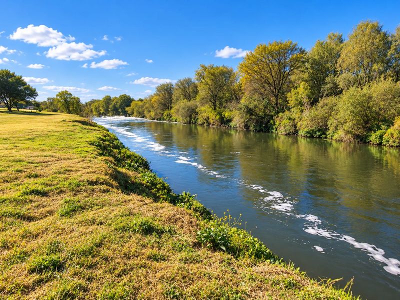 A scenic view of a river flowing alongside a grassy bank, showcasing the natural beauty and waterfront potential of the vacant land.
