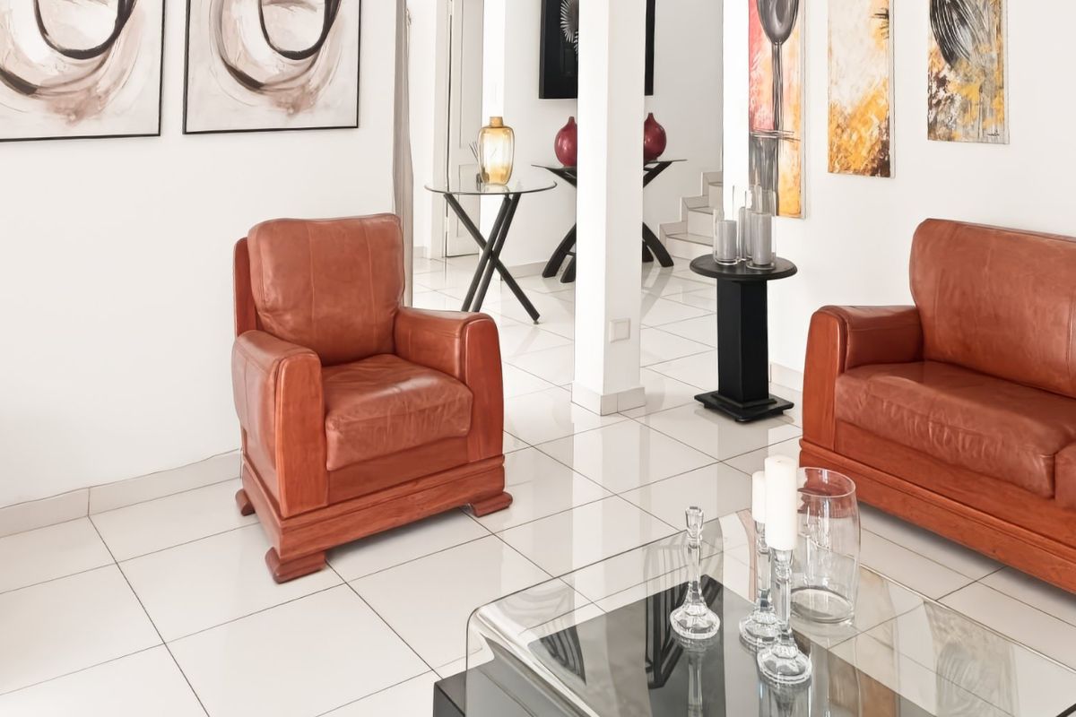 A bright living room featuring polished white floor tiles and a central structural column, creating an open and airy atmosphere.