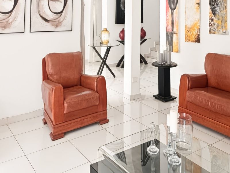 A bright living room featuring polished white floor tiles and a central structural column, creating an open and airy atmosphere.