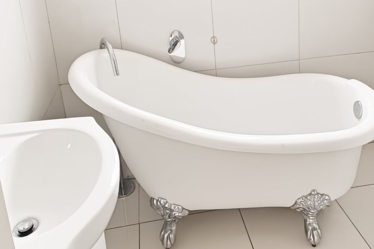 A clean bathroom featuring a classic white clawfoot bathtub with chrome fixtures and a matching pedestal basin, finished with neutral ceramic tiling.