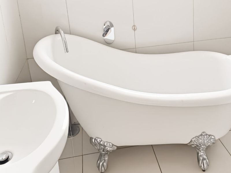 A clean bathroom featuring a classic white clawfoot bathtub with chrome fixtures and a matching pedestal basin, finished with neutral ceramic tiling.