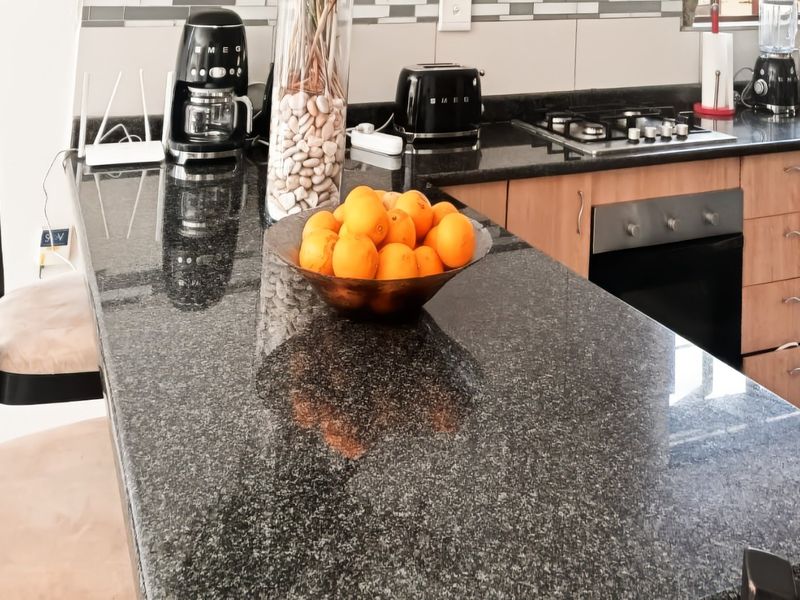 A functional kitchen featuring granite countertops, wooden cabinetry, a built-in oven, and a gas hob with a tiled backsplash.