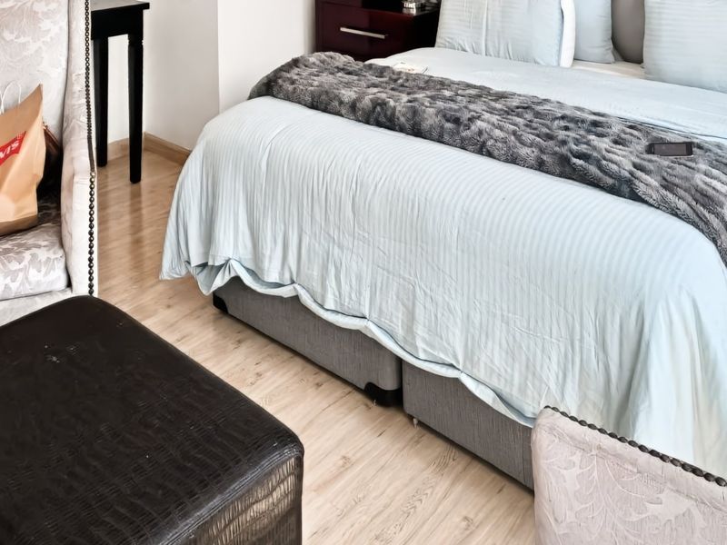 A well-maintained bedroom featuring light-toned laminate flooring and a neutral color palette.