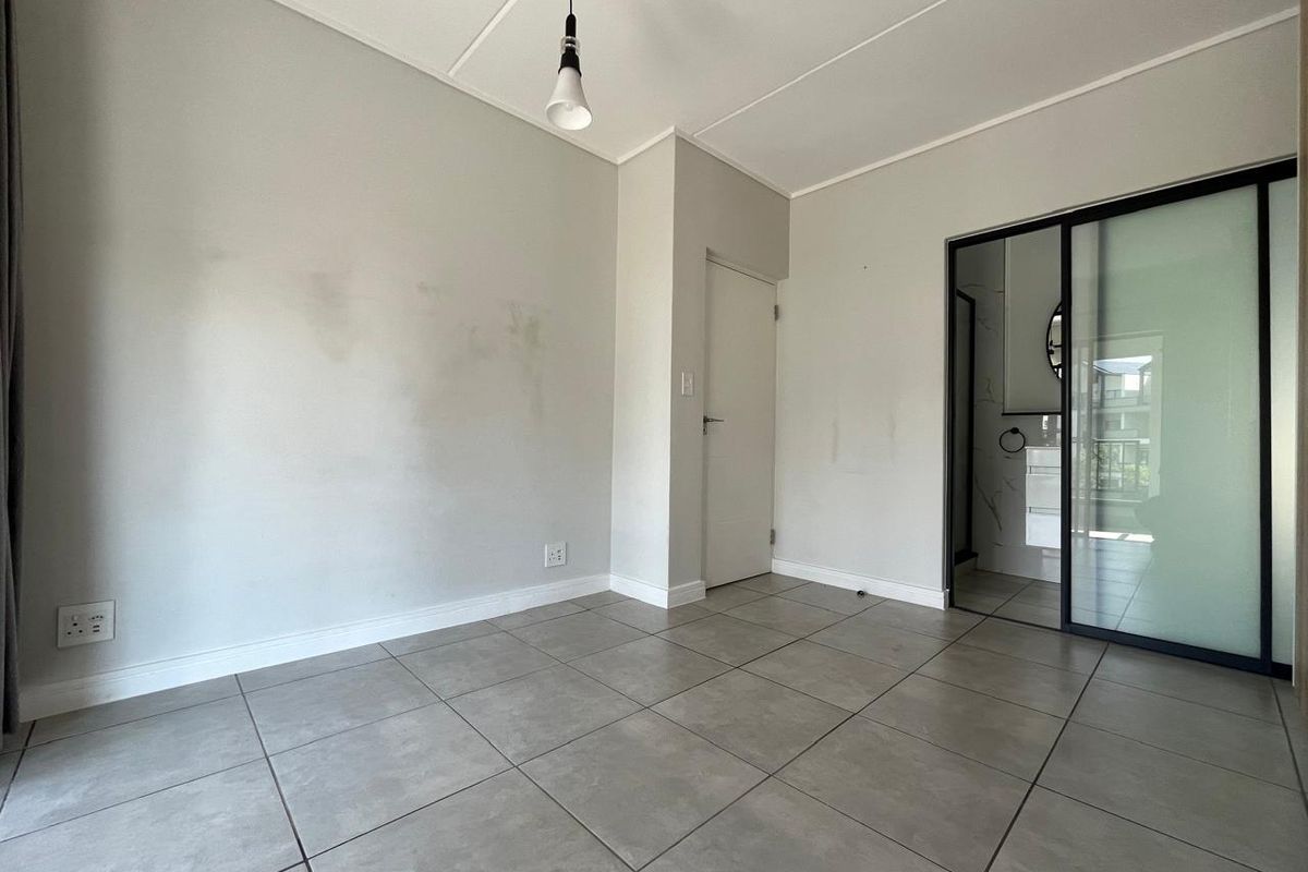 An empty bedroom featuring neutral tiled flooring, a modern sliding glass door leading to an en-suite, and a minimalist pendant light fixture.