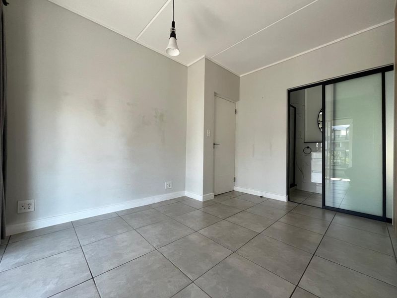 An empty bedroom featuring neutral tiled flooring, a modern sliding glass door leading to an en-suite, and a minimalist pendant light fixture.
