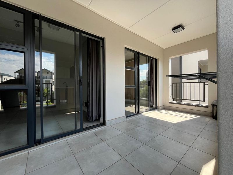 A clean, modern balcony featuring tiled flooring, sliding glass doors, and a wall-mounted drying rack, offering a bright and functional outdoor space.