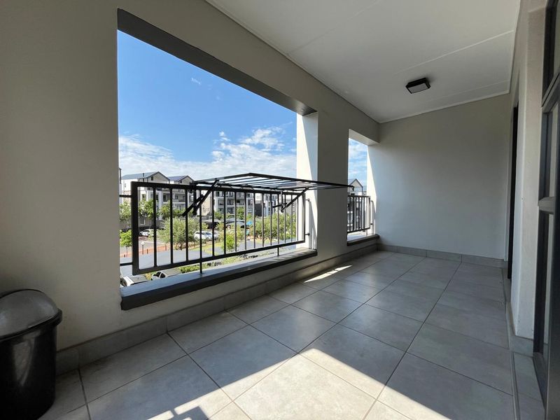 A clean, tiled balcony featuring a metal balustrade and a wall-mounted drying rack, offering an open view of the surrounding residential complex.