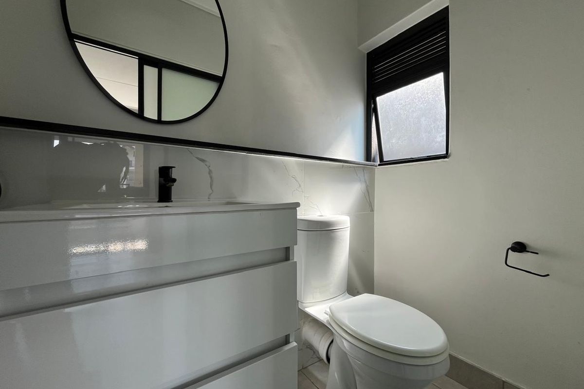 Modern bathroom featuring a sleek white vanity with black tapware, marble-look splashback, and a contemporary toilet.