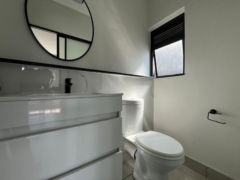 Modern bathroom featuring a sleek white vanity with black tapware, marble-look splashback, and a contemporary toilet.