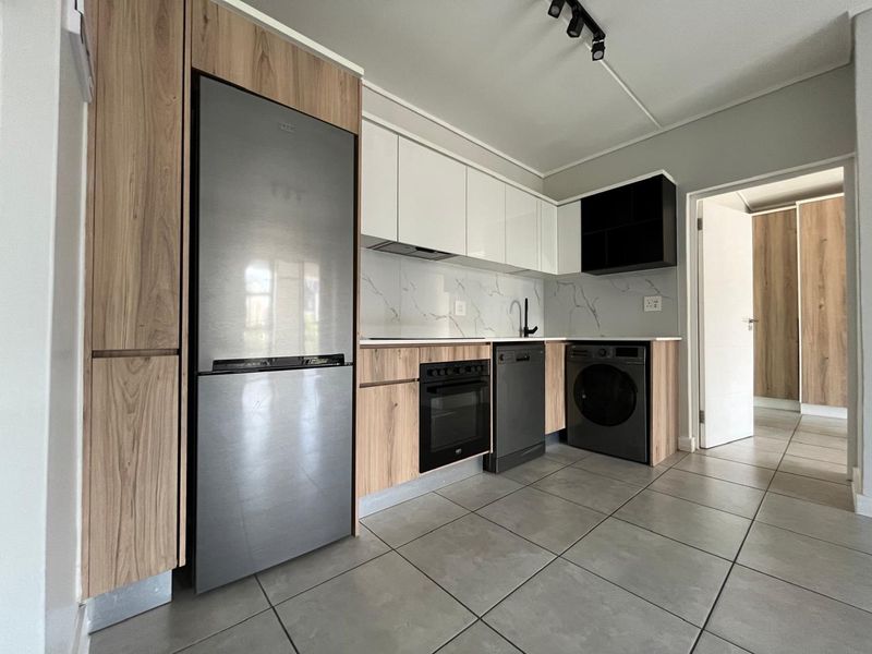Modern kitchen featuring sleek wood-grain and white cabinetry, marble-look splashback, integrated appliances, and contemporary track lighting.