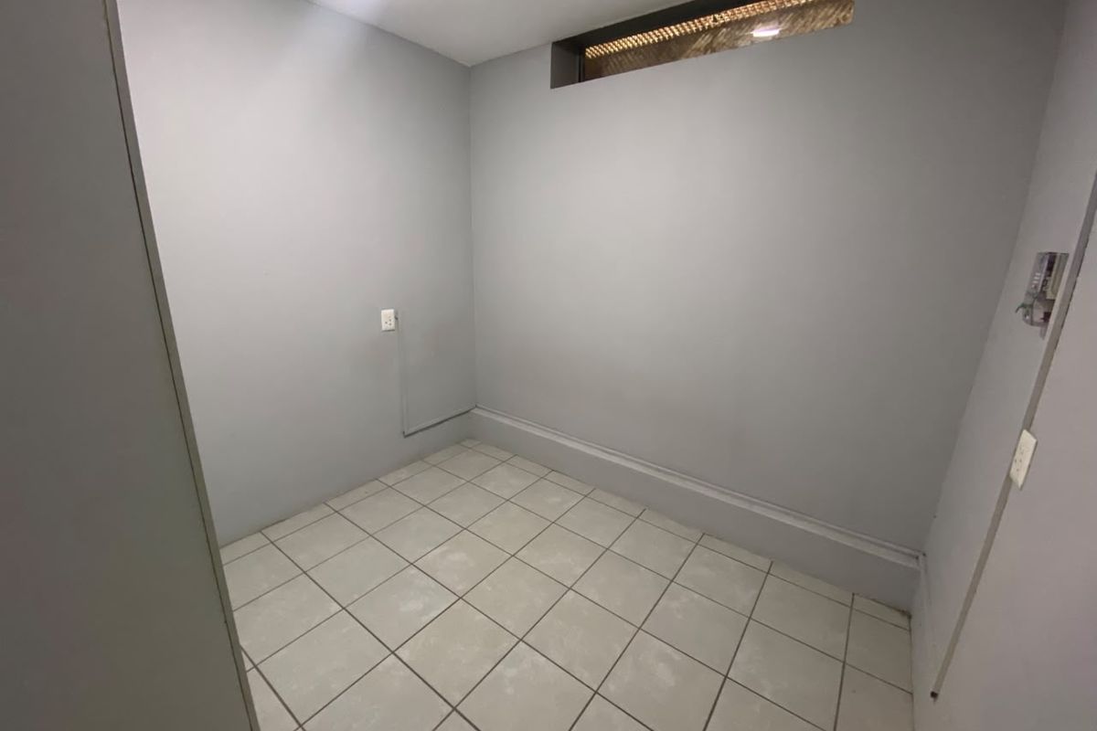 A compact, empty room featuring neutral grey walls, tiled flooring, and a high-level clerestory window, suitable for a bedroom or home office.