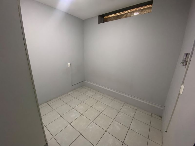 A compact, empty room featuring neutral grey walls, tiled flooring, and a high-level clerestory window, suitable for a bedroom or home office.