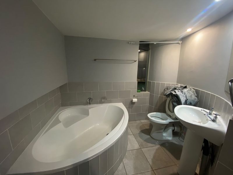 A functional bathroom featuring a corner bathtub, pedestal basin, and toilet with neutral wall and floor tiling.