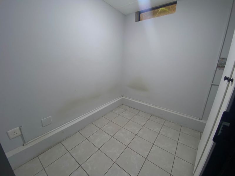 A small, empty utility space featuring tiled flooring and a high-level window, showing visible signs of wall staining.
