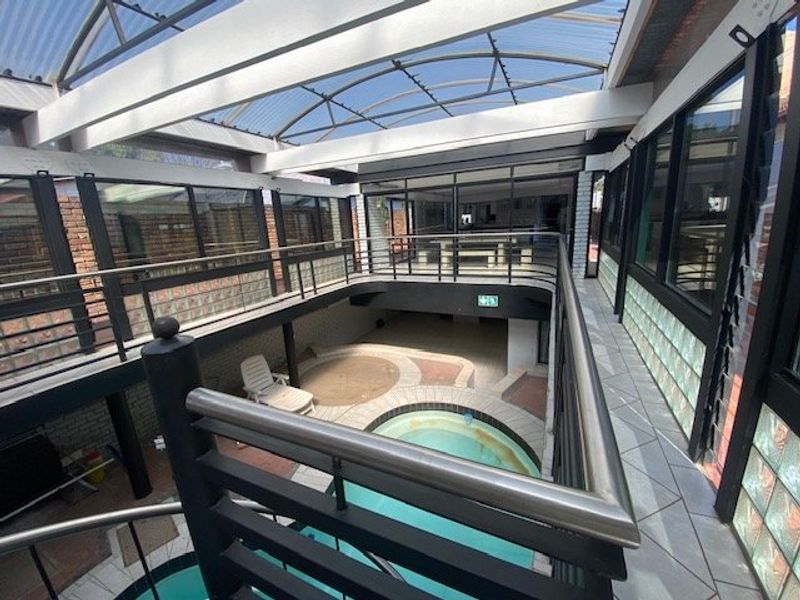 An indoor swimming pool area featuring a covered polycarbonate roof, metal balustrades, and glass block wall accents, providing a unique enclosed entertainment space.