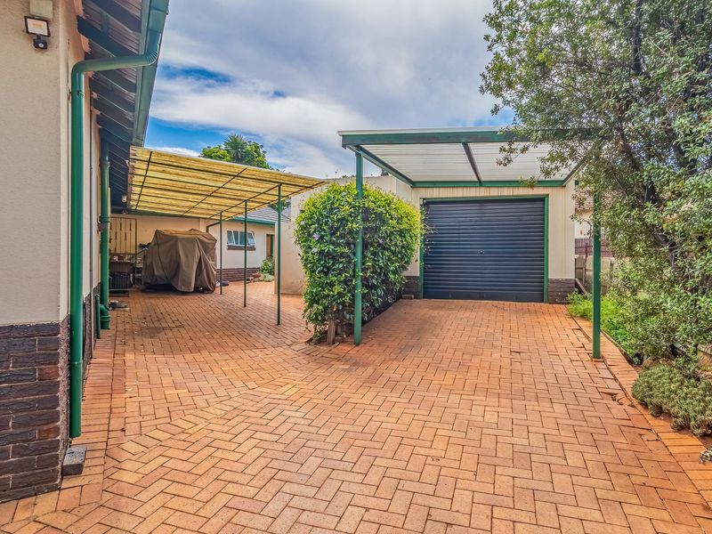Rear exterior view featuring brick paved driveway, covered carport area, and a single garage with a roller door.