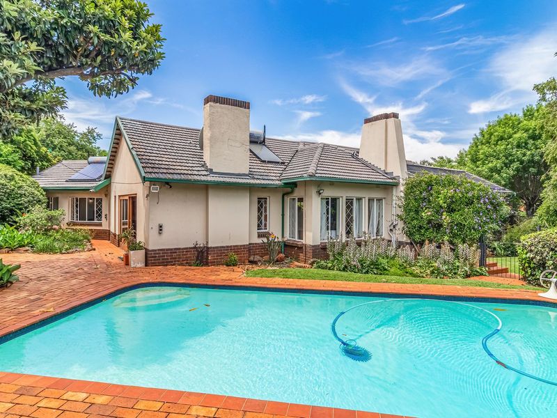 A well-maintained rear exterior view featuring a swimming pool, brick paved patio, and a tiled roof house with prominent chimneys.