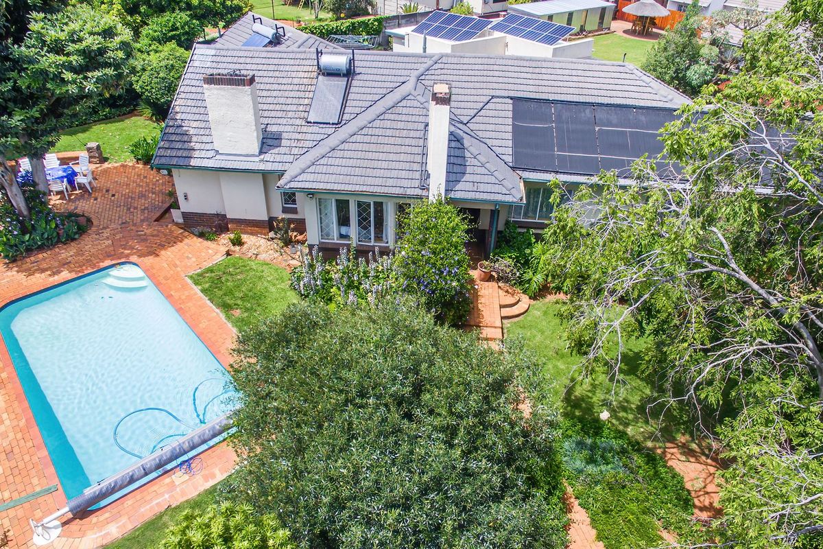 Aerial view of a residential property featuring a swimming pool, brick paved patio, solar panels, and a well-maintained garden.