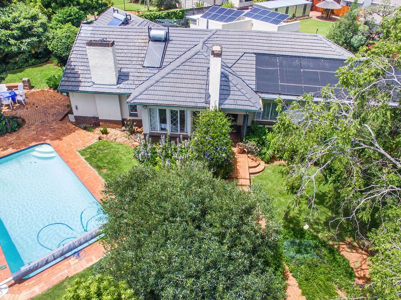 Aerial view of a residential property featuring a swimming pool, brick paved patio, solar panels, and a well-maintained garden.