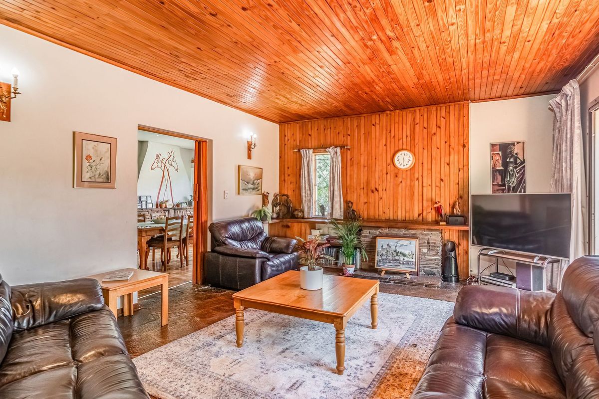 Spacious living room featuring a distinctive timber-paneled ceiling, warm wood wall accents, a stone fireplace, and durable stone flooring with access to the outdoors.