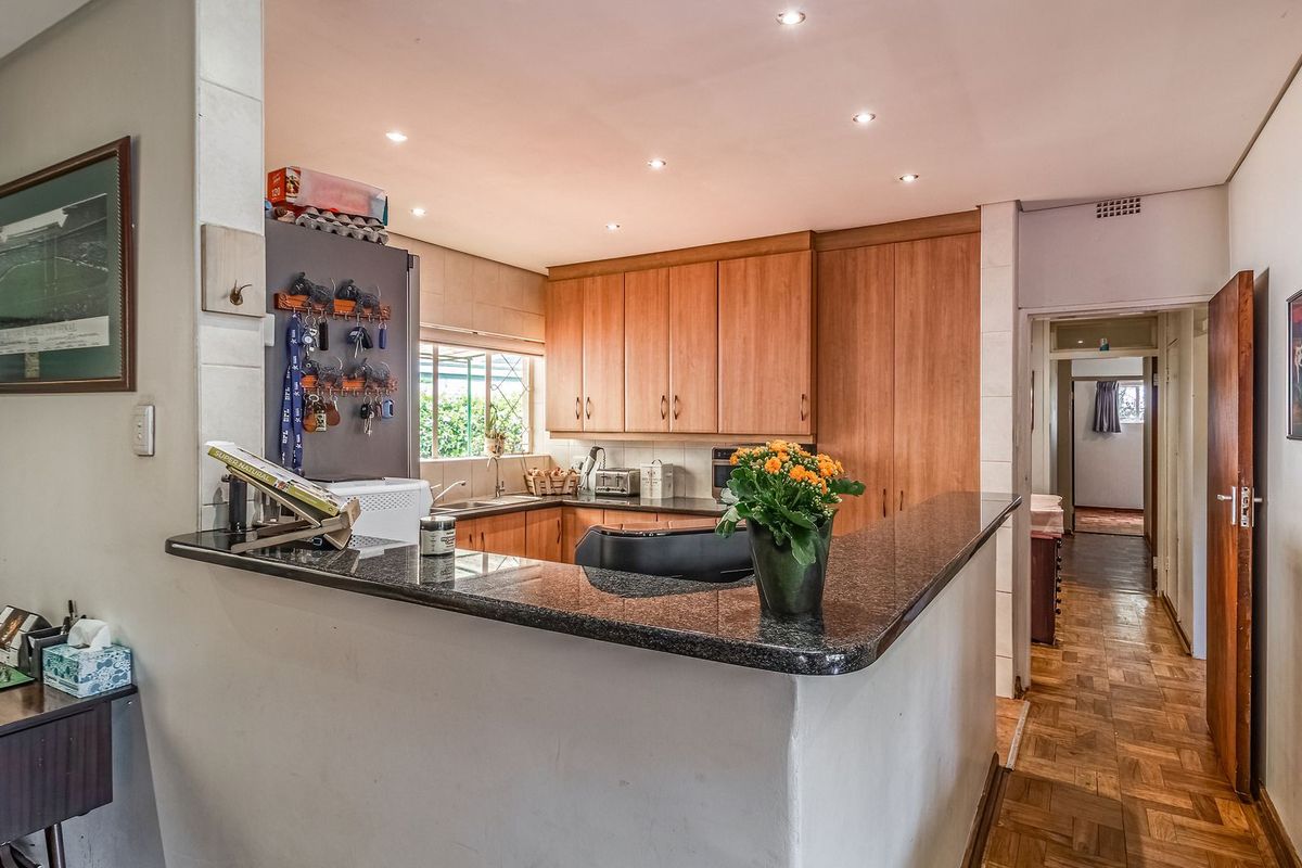 Functional kitchen featuring wooden cabinetry, granite countertops, and parquet flooring, with an open-plan layout connecting to the adjacent living area.
