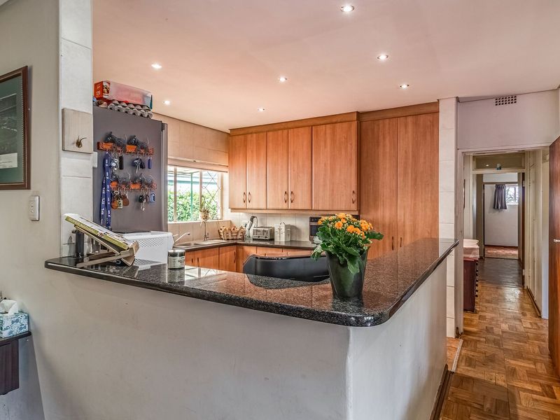 Functional kitchen featuring wooden cabinetry, granite countertops, and parquet flooring, with an open-plan layout connecting to the adjacent living area.