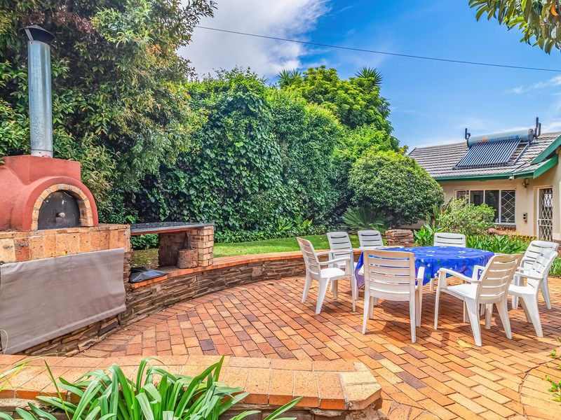 A spacious outdoor patio featuring a built-in brick pizza oven and braai area, perfect for entertaining in a private garden setting.