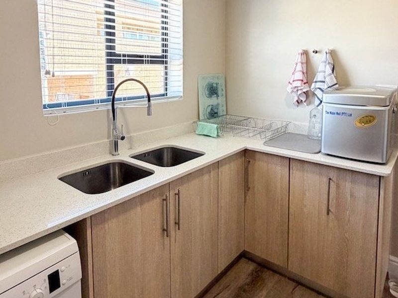 A functional laundry area featuring light wood-finish cabinetry, stone countertops, and a double stainless steel sink with a modern mixer tap.