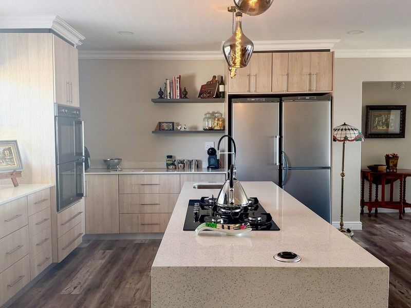 Modern kitchen featuring a large central island with a gas hob, stone countertops, light wood cabinetry, and high-quality finishes throughout.