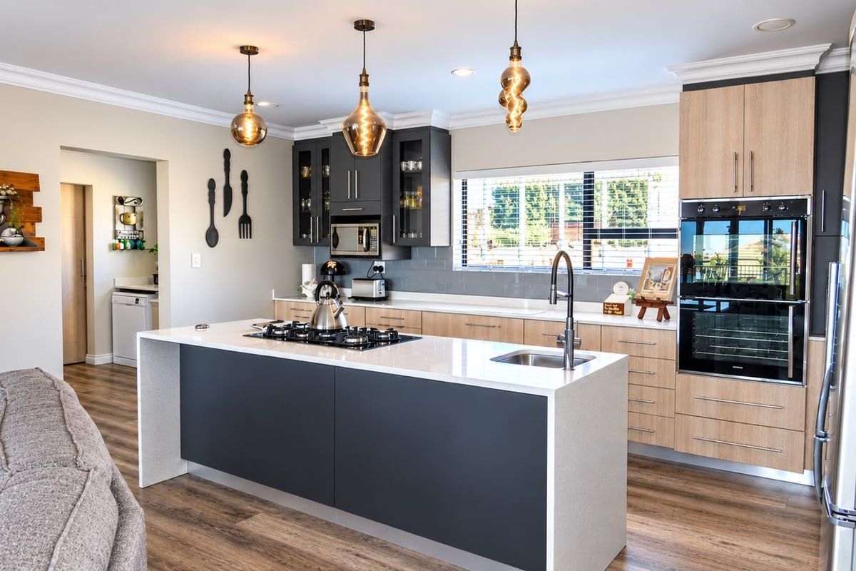 Modern kitchen featuring a central island with gas cooktop, quartz countertops, built-in double oven, and contemporary cabinetry with stylish pendant lighting.