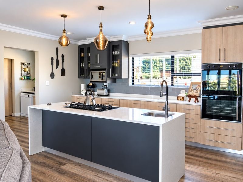 Modern kitchen featuring a central island with gas cooktop, quartz countertops, built-in double oven, and contemporary cabinetry with stylish pendant lighting.
