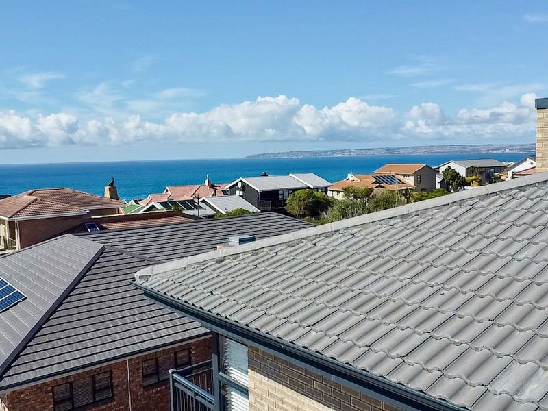 Elevated coastal view overlooking residential rooftops, featuring tiled roofing, solar panels, and a brick chimney with the ocean in the background.