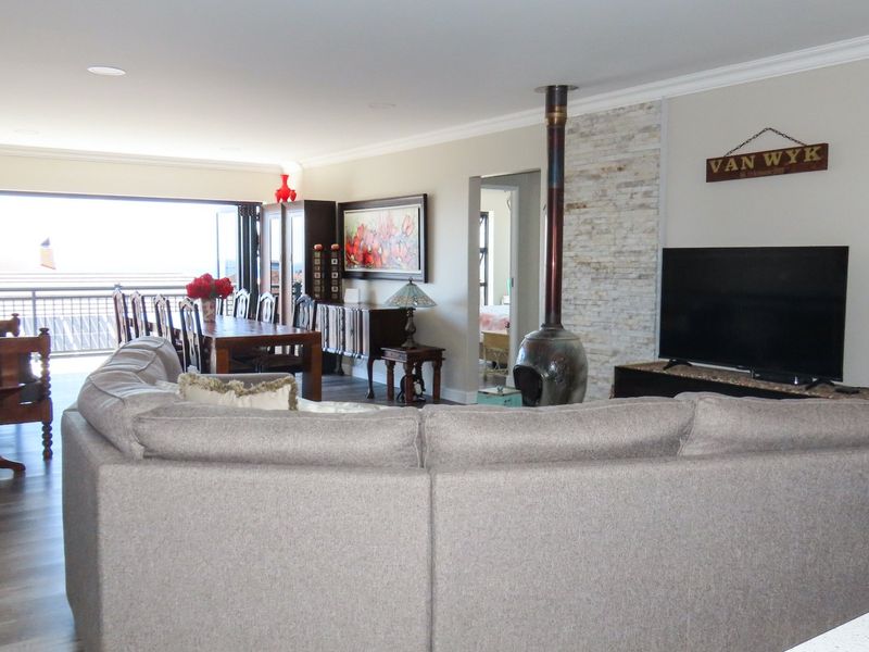 Spacious open-plan living and dining area featuring a stone-clad fireplace, modern laminate flooring, and large sliding doors leading to an outdoor balcony.