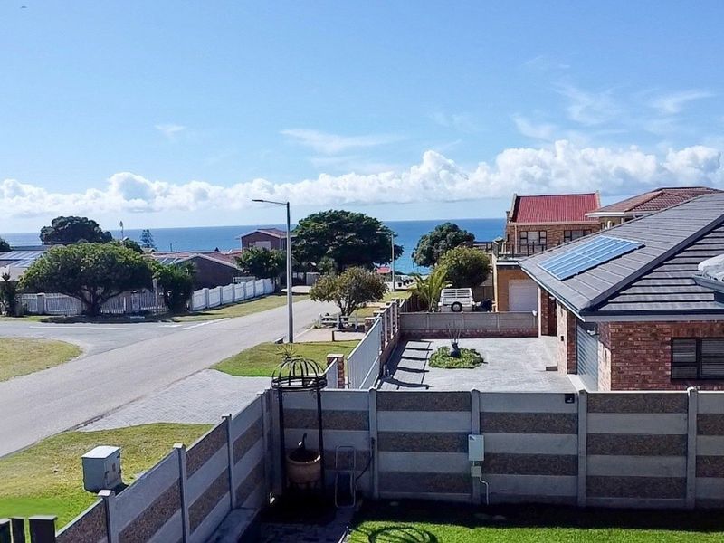 Elevated view overlooking a residential street and neighbourhood with a distant ocean horizon and clear blue sky.